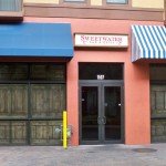 The rear entrance to Sweetwater Bar & Grill with empty storefronts on either side and apartments above.